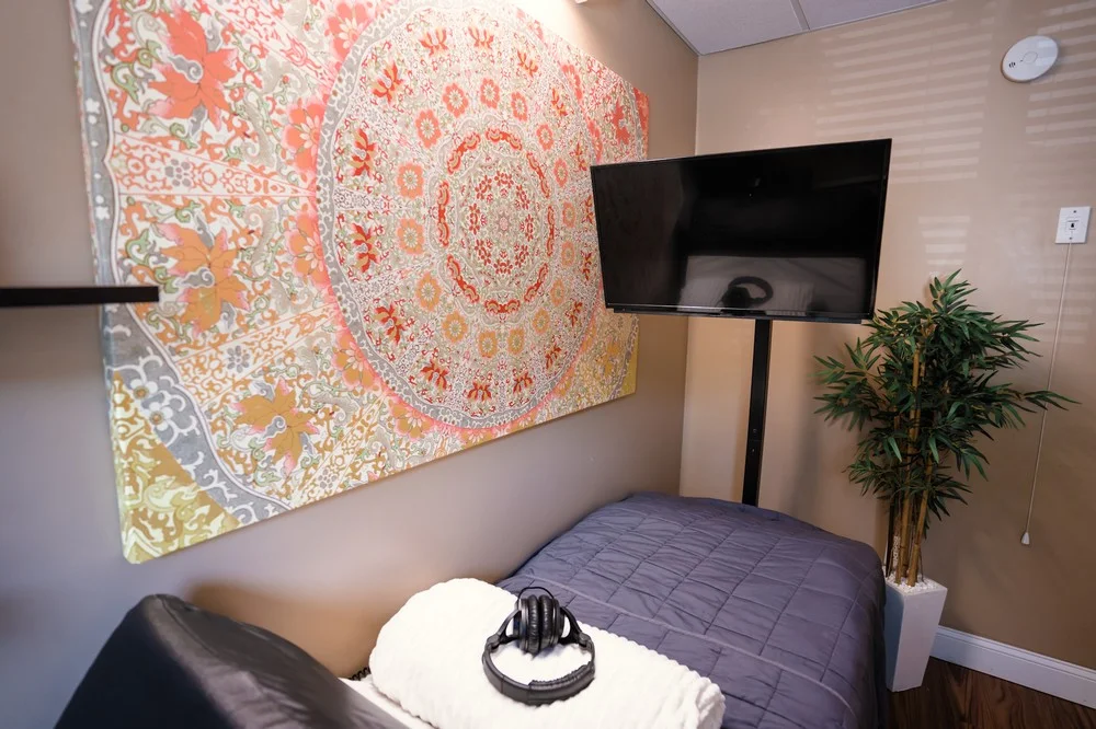 DSC09601-22 Room with patterned tapestry, TV on wall, blue bed, plant, and headphones on white towel.