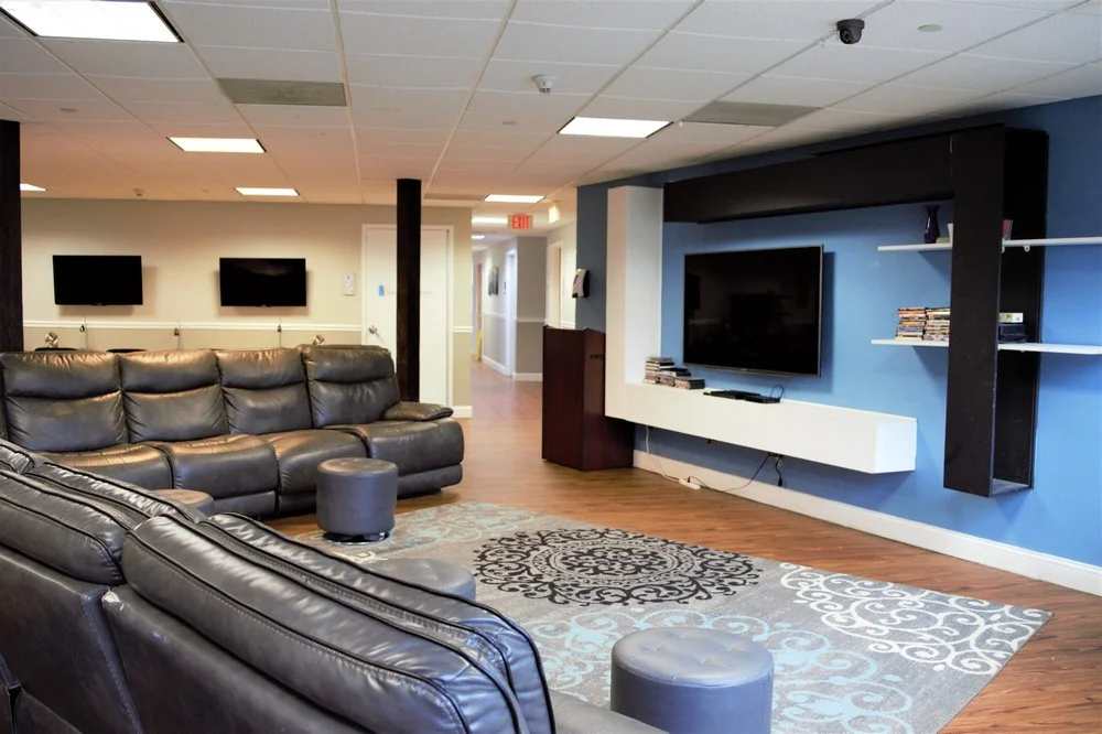 L1COUCHBROCHURE Spacious lounge with leather sofas, flat-screen TVs, blue accent wall, and patterned rug.