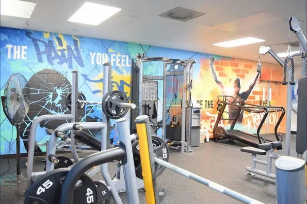 ezgif-2-9b7a6f142d@2x Gym interior with weightlifting equipment, treadmill, and motivational wall murals.