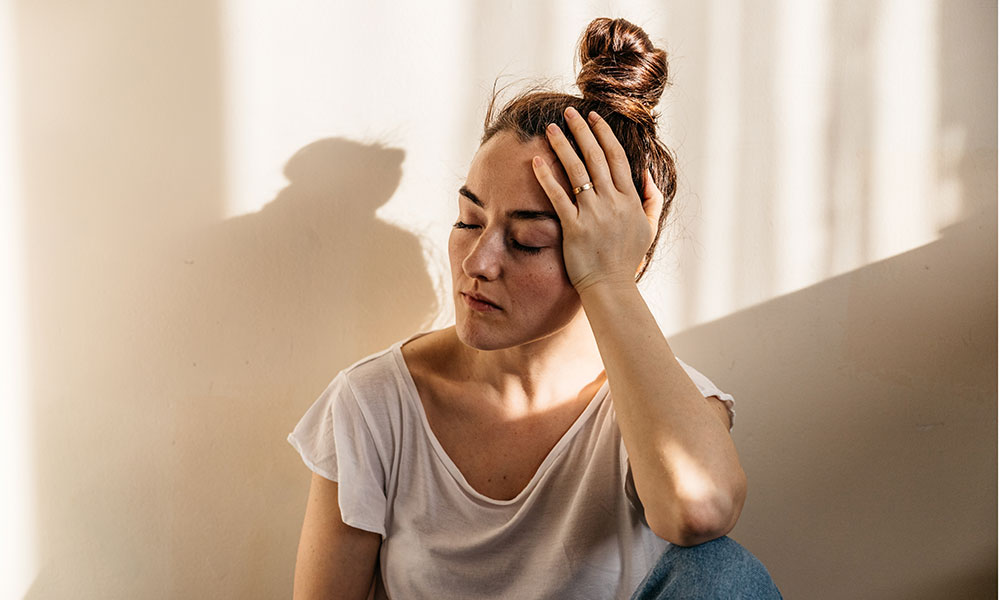 Person in a white shirt sitting with hand on head looking pensive.