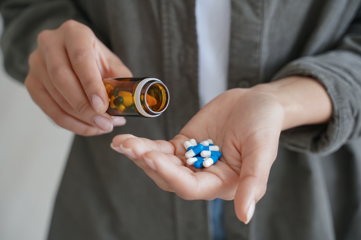 Person holding pill bottle and blue capsules.