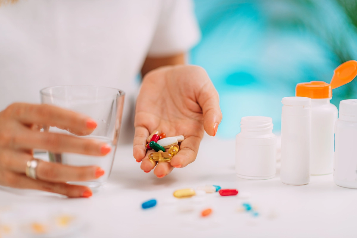 Person holding pills and a glass of water on a table with pill bottles.