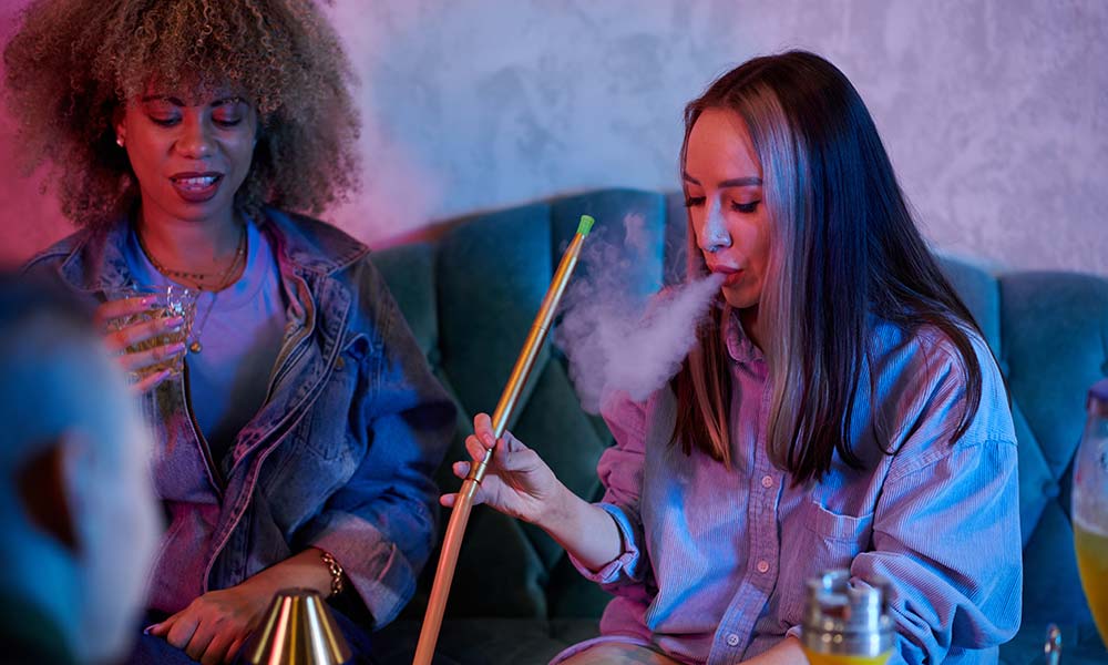 woman smoking from a hookah, while the other woman having alcohol.