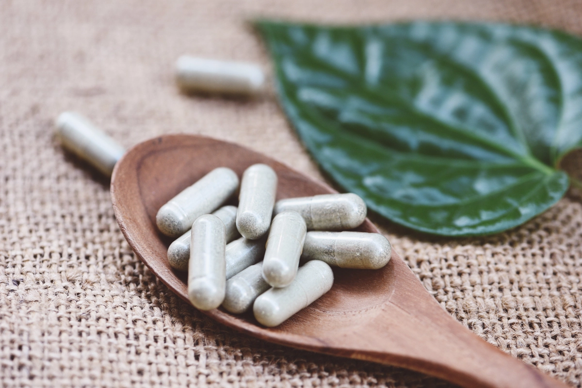 Herbal capsules on a wooden spoon with green leaf background.