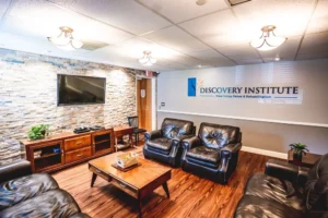 DSC00781-119-Recovered-2 Lobby with leather chairs, TV, wooden furniture, and Discovery Institute New Jersey Detox & Rehabilitation sign.